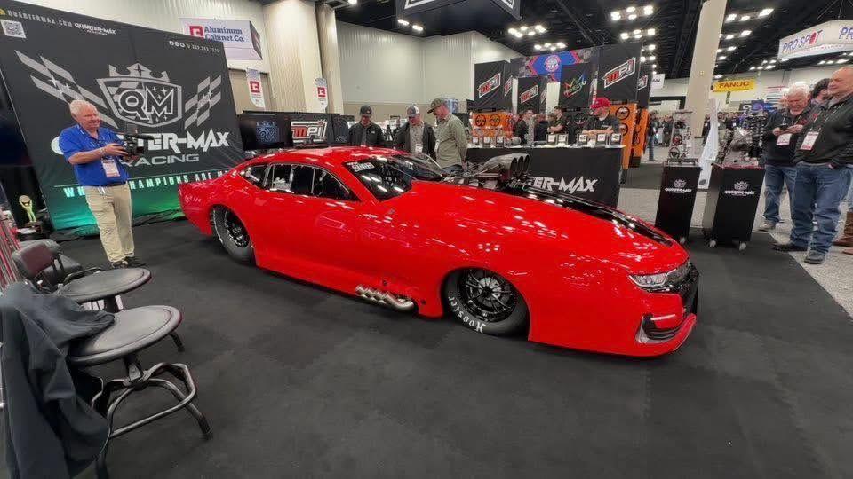Bright red sports car on display at an auto show with people and banners in the background