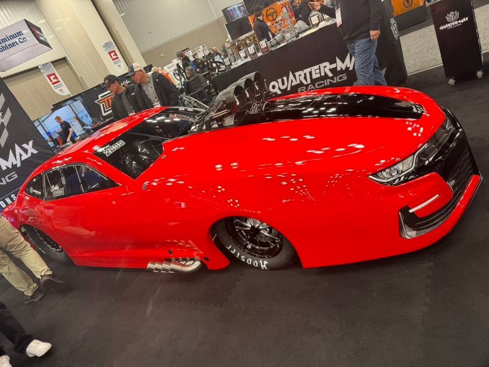 Red sports car on display at an auto show, viewed from the side.