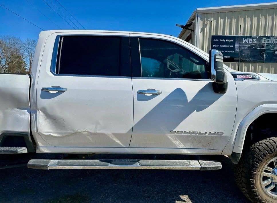 White pickup truck with visible side damage, parked outdoors in bright sunlight.