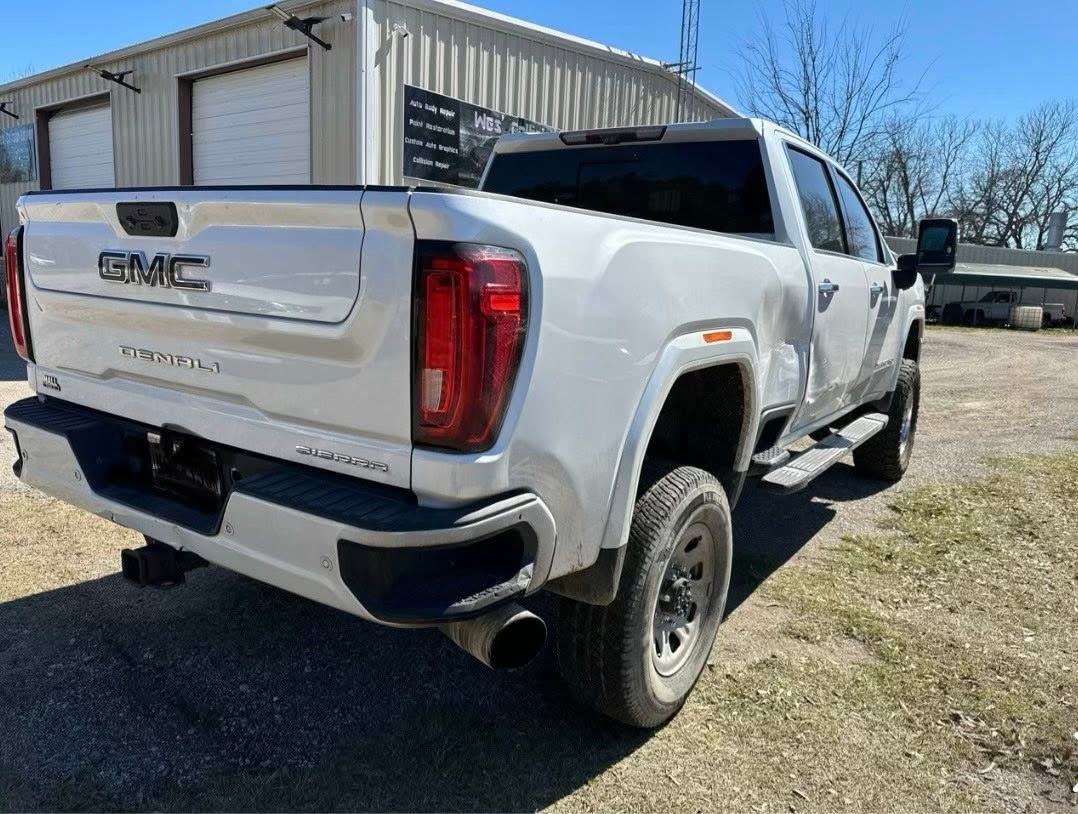 White GMC Sierra pickup parked beside a metal building on a gravel lot, rear three-quarter view
