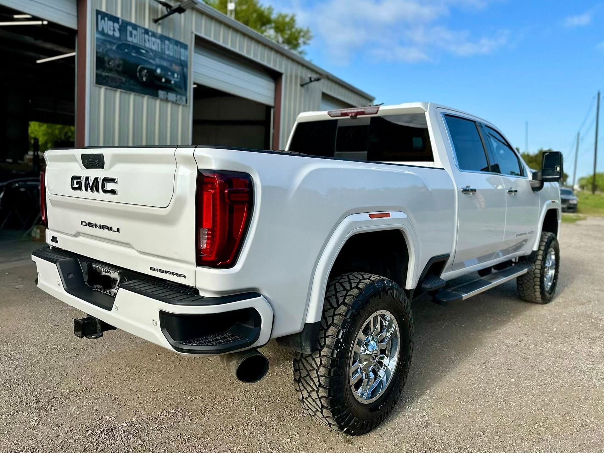 White GMC Denali HD pickup truck parked outside a garage, rear three-quarter view