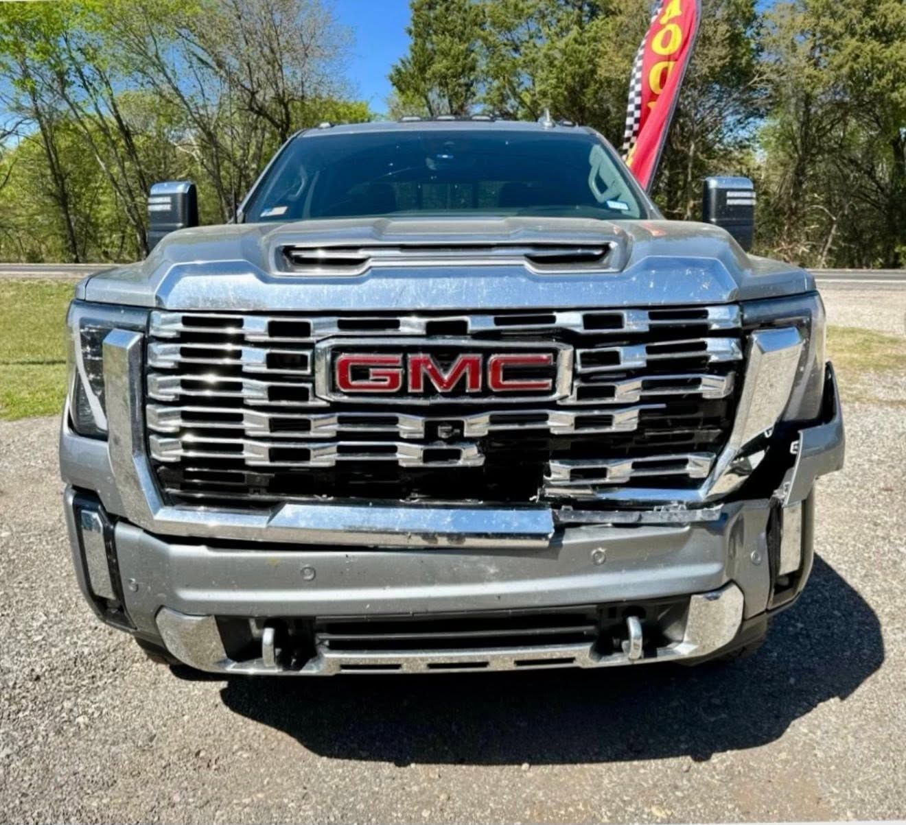 Front view of a silver GMC pickup truck on a lot, with chrome grille and trees in the background