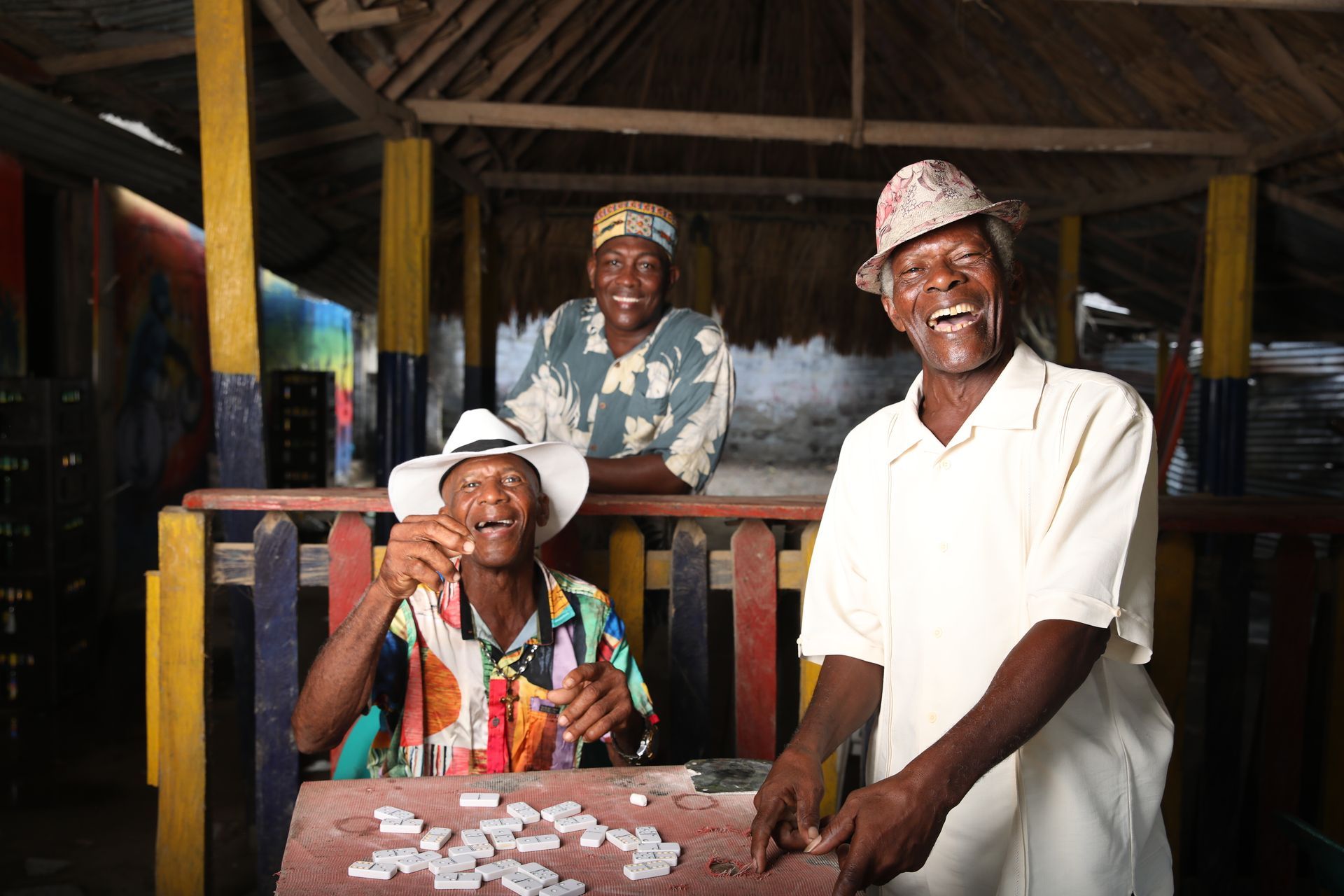 Tres personas sonriendo detrás de una mesa cubierta de monedas esparcidas en un refugio rústico de madera.