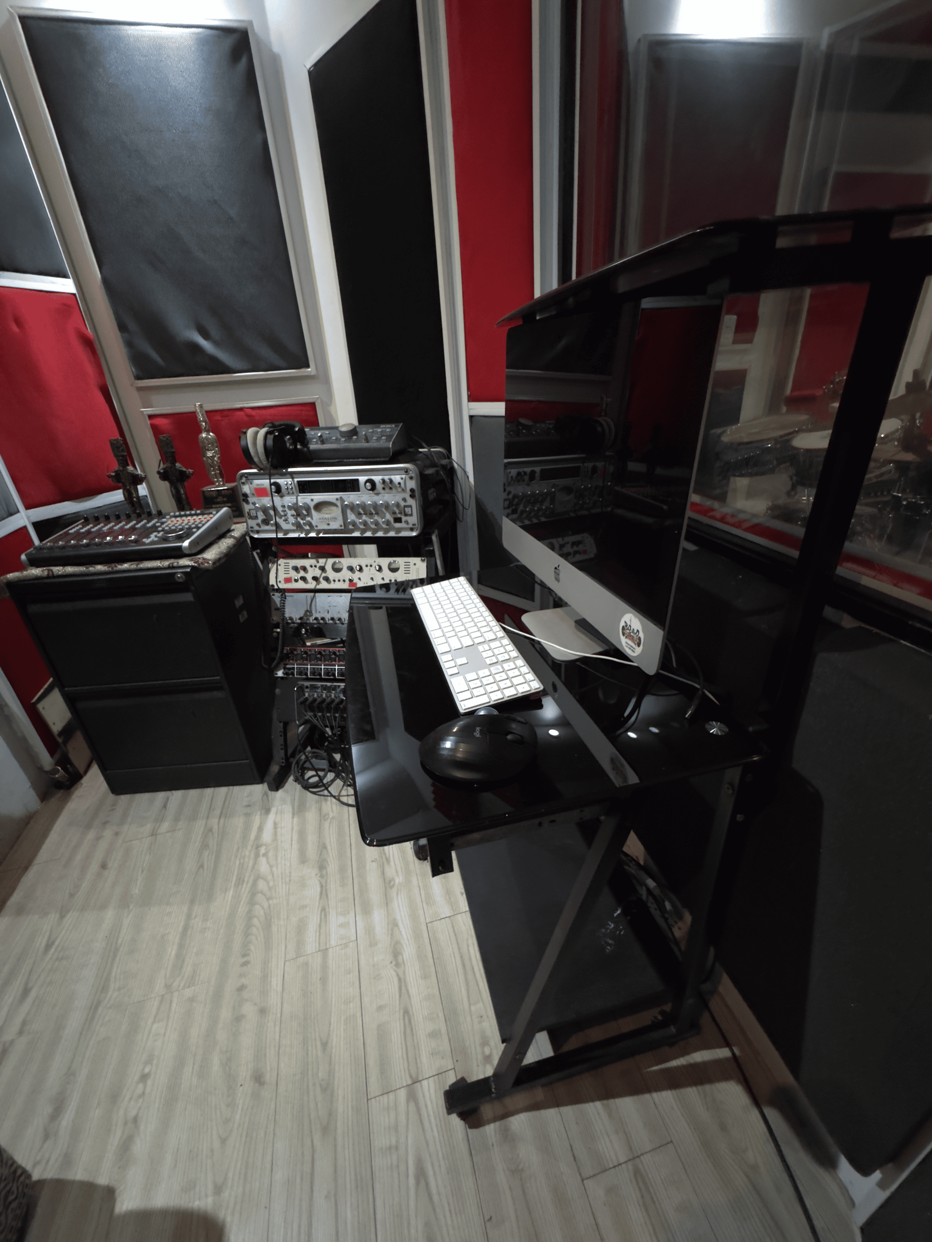 Pequeño estudio de música con piano digital, equipo de audio y paneles acústicos a lo largo de paredes rojas y negras.