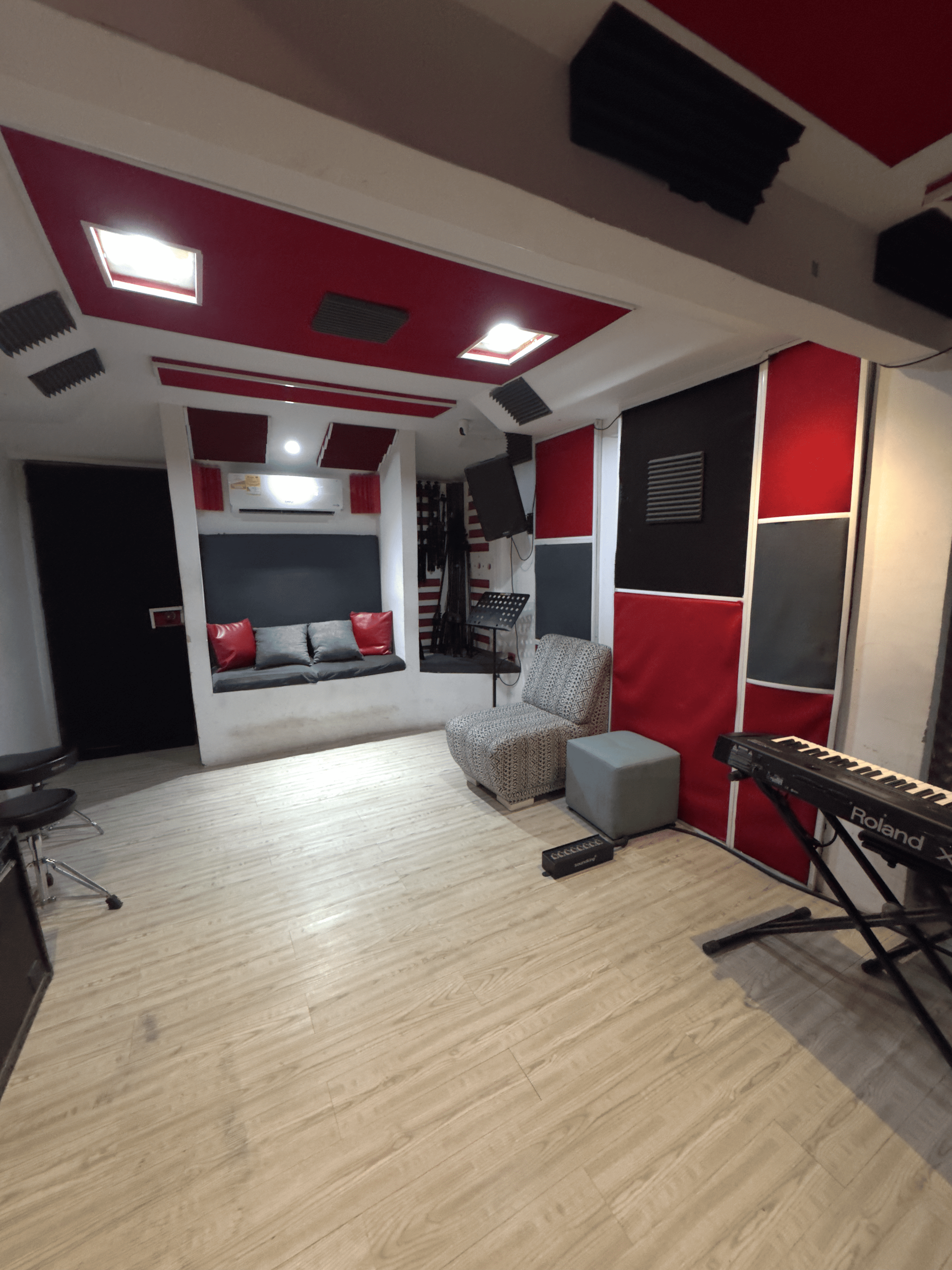 Estudio de grabación insonorizado con paneles acústicos rojos y negros, teclado y zona de estar.