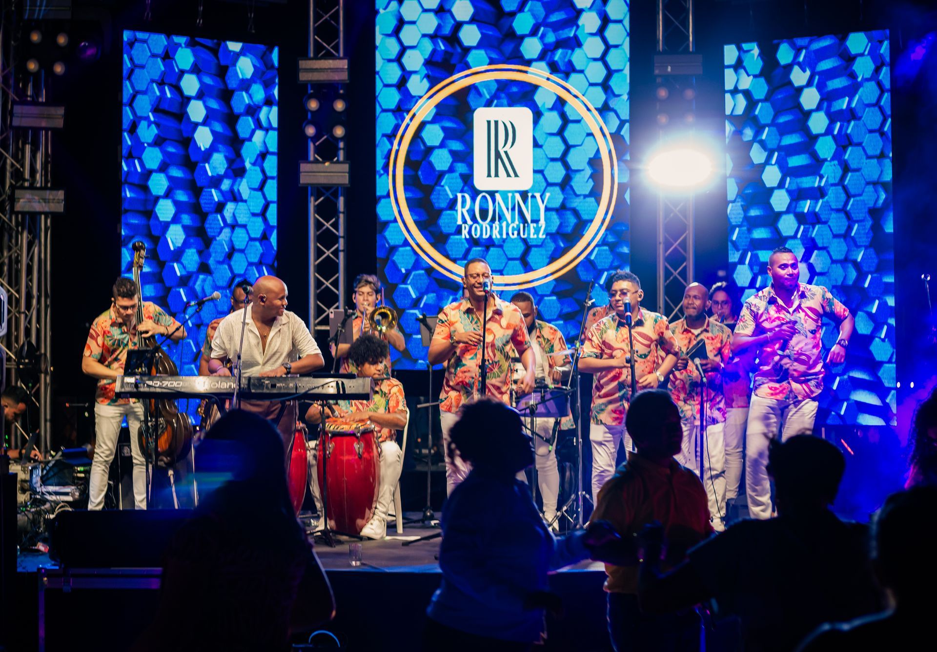 Banda en vivo actuando en un escenario iluminado con luz azul, con tambores de conga
