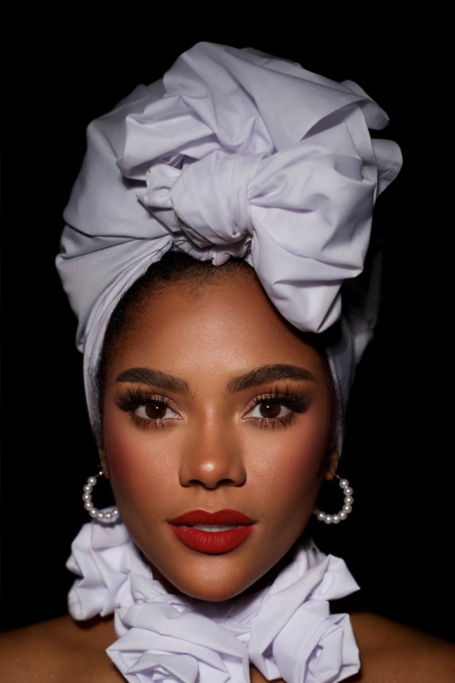 Retrato de una persona con un turbante blanco y un cuello blanco con volantes sobre un fondo negro.