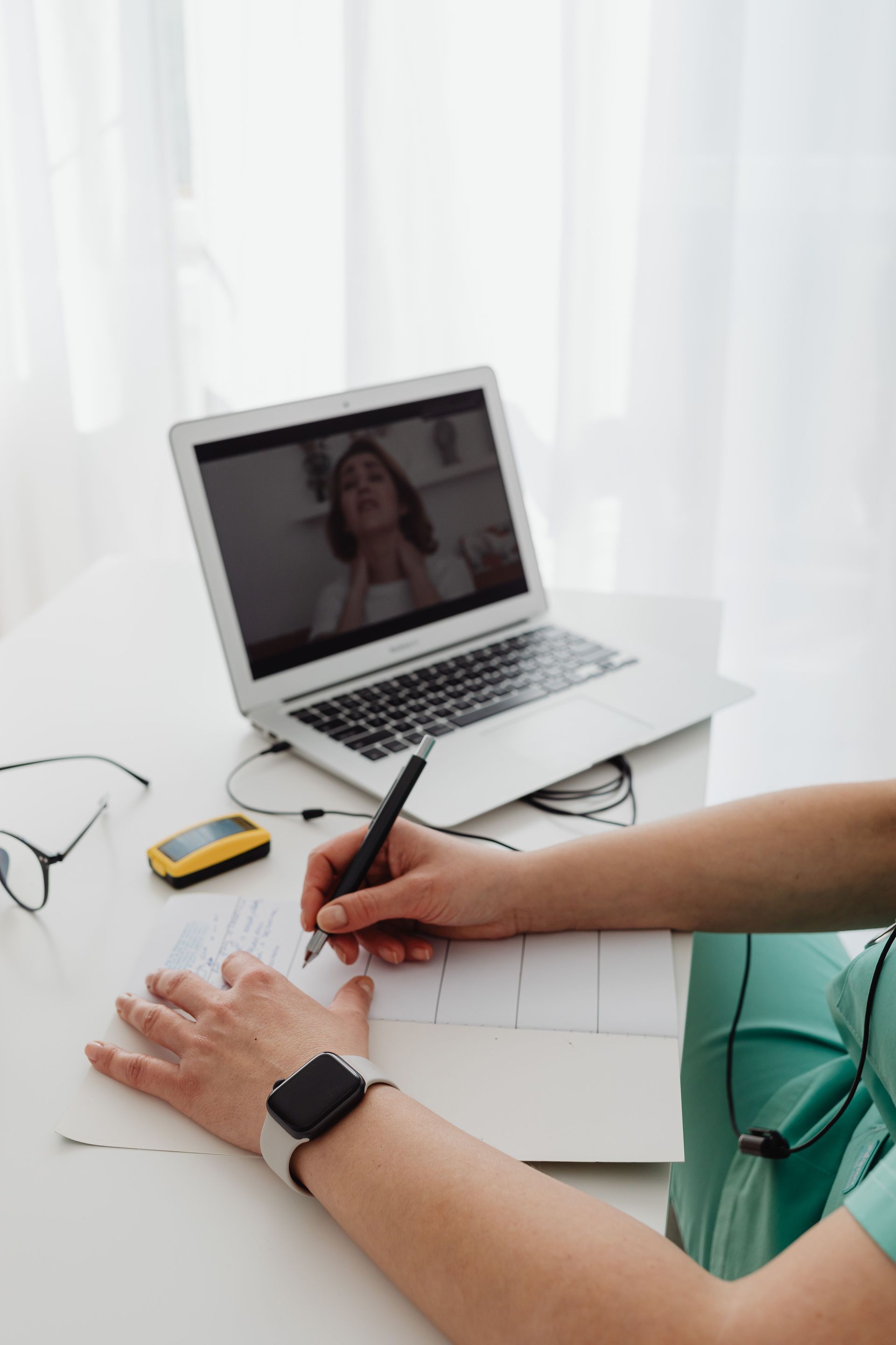Person writing in a notebook at a desk with a laptop open on a video call