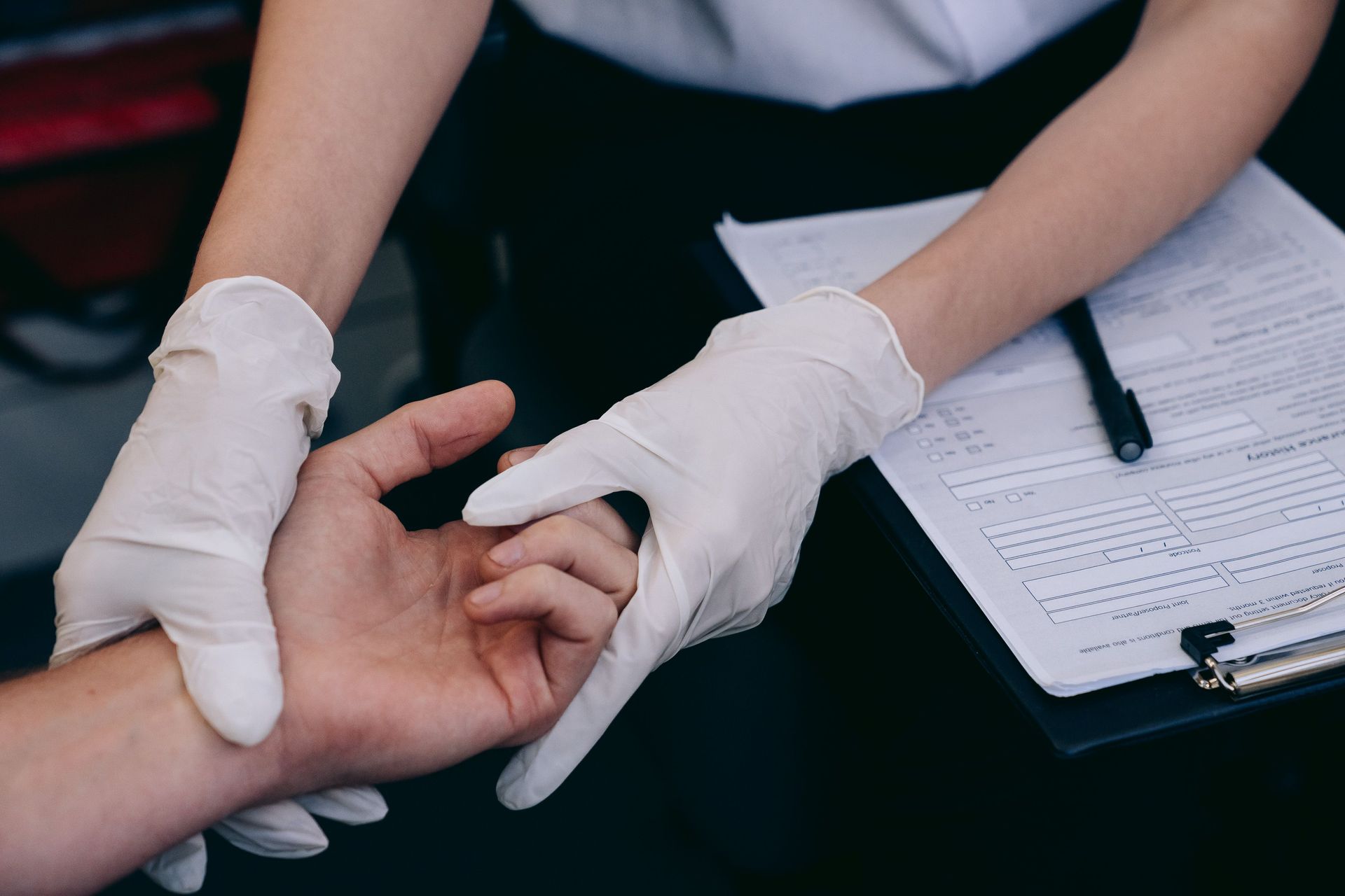 Gloved hands checking a person’s wrist with paperwork and clipboard nearby