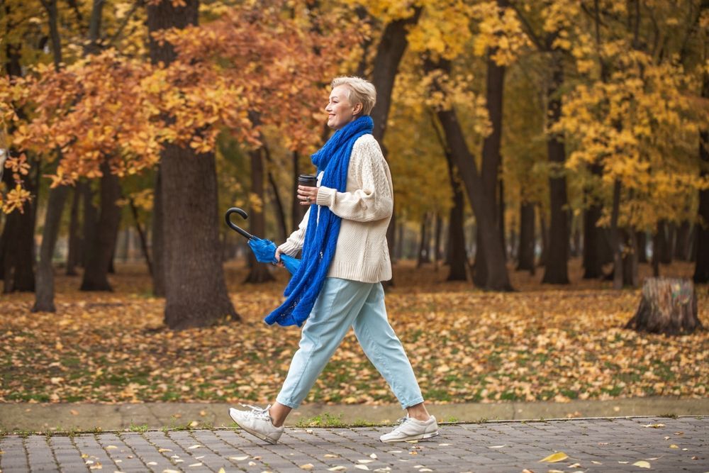A happy middle-aged woman walking through a park with a coffee.