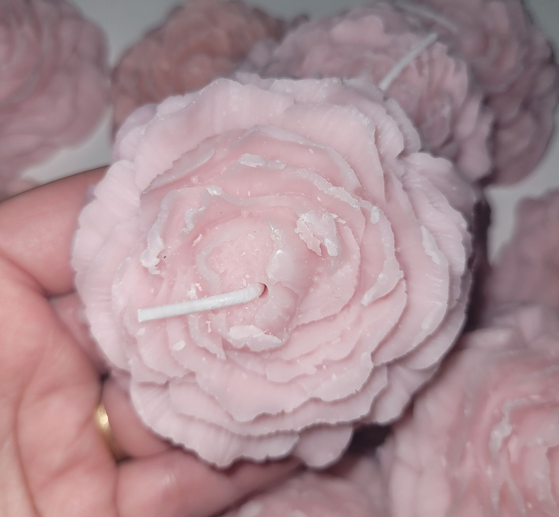 Hand die een lichtroze, bloemvormige kaars vasthoudt met gelaagde bloemblaadjes en een zichtbare lont.
