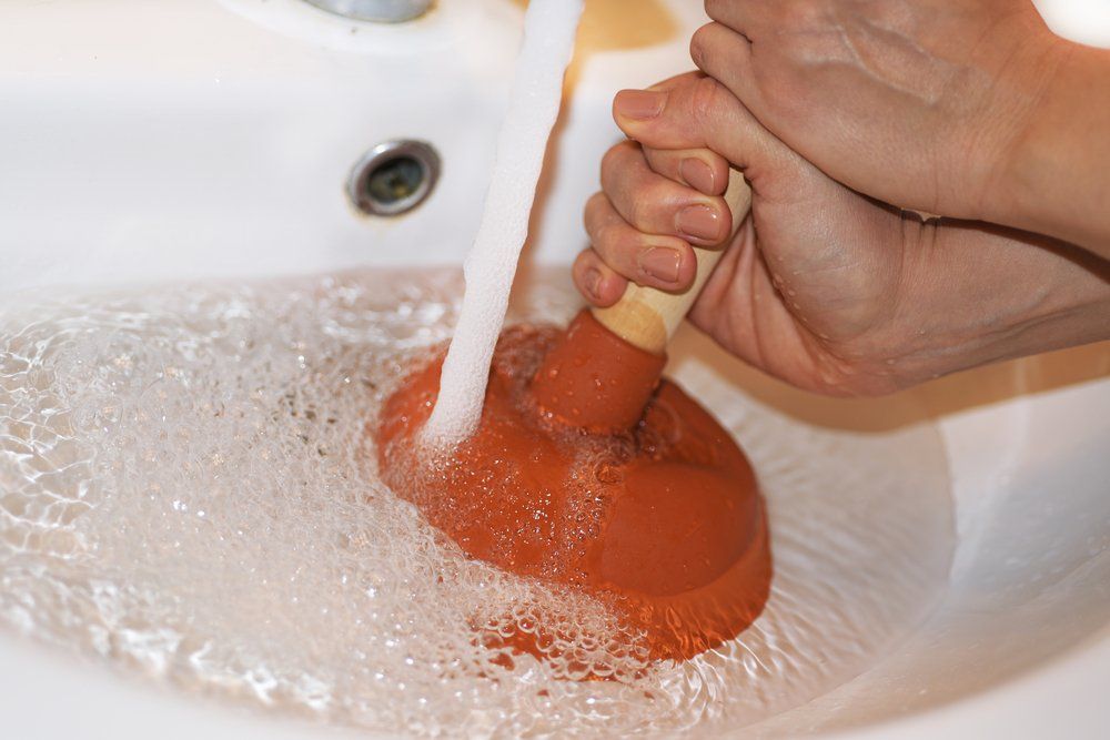 A Person is Using a Plunger to Unblock a Drain in a Sink — Greg Mitchell Plumbing In Murgon, QLD