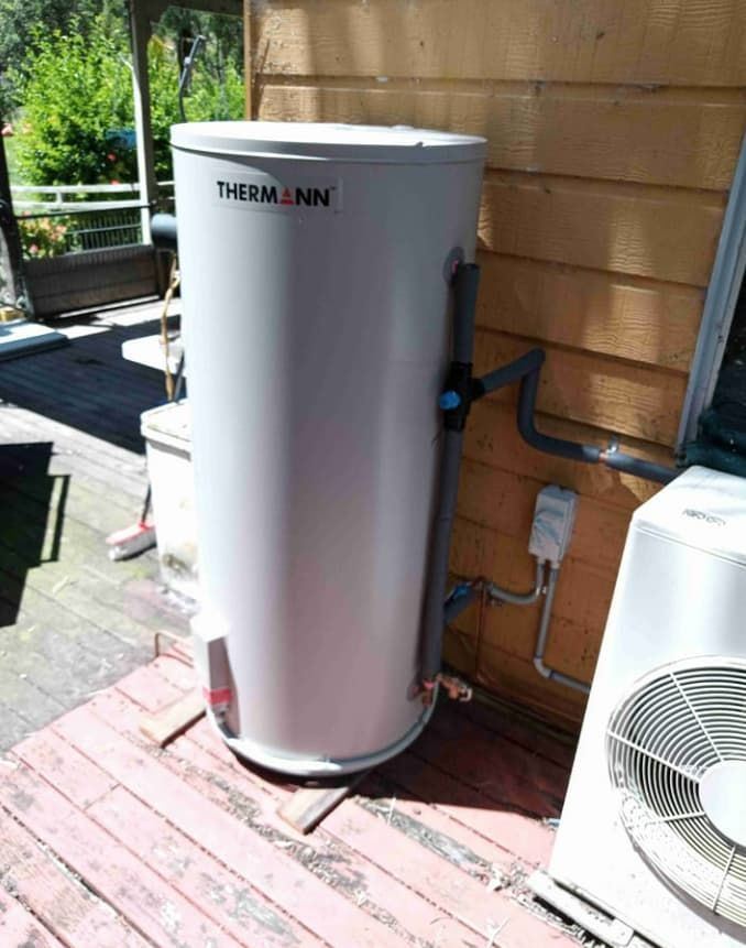A White Water Heater is Sitting on a Wooden Deck Next to a Fan — Greg Mitchell Plumbing In Nanango, QLD