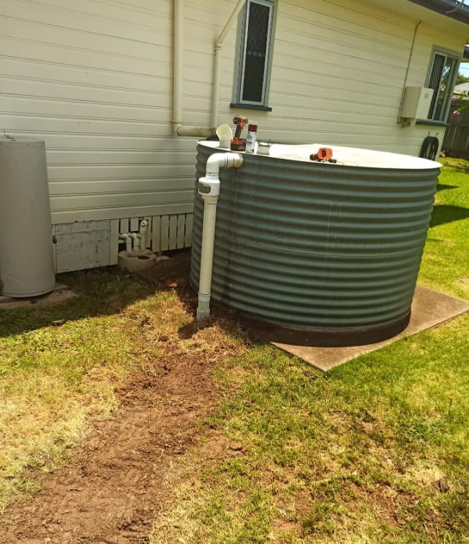 A Large Metal Tank is Sitting in the Grass in Front of a House — Greg Mitchell Plumbing In Wondai, QLD