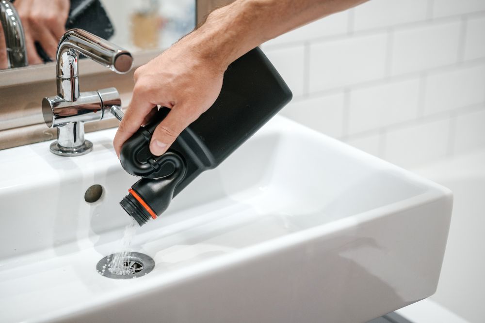 A Person is Pouring a Bottle of Drain Cleaner Into a Bathroom Sink — Clinton McArthur Plumbing in Caloundra, QLD