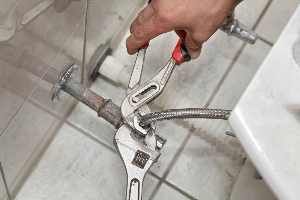 A Person is Fixing a Pipe With a Wrench in a Bathroom — Clinton McArthur Plumbing in Glenview, QLD
