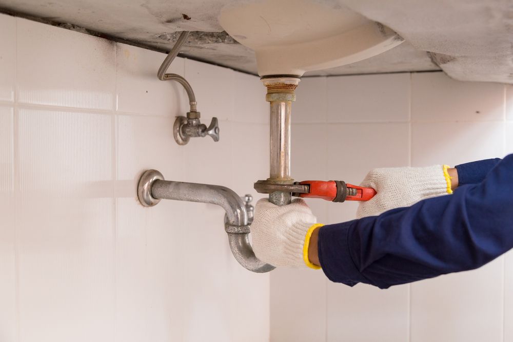 A Plumber is Fixing a Sink Pipe With a Wrench — Clinton McArthur Plumbing in Maroochydore, QLD