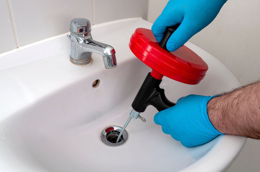 A Person is Using a Drain Snake to Unblock a Sink — Clinton McArthur Plumbing in Maroochydore, QLD