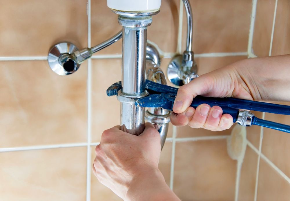 A Person is Fixing a Sink Pipe With a Wrench — Clinton McArthur Plumbing in Landsborough, QLD