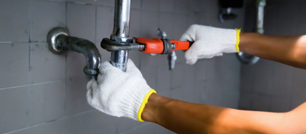 A Plumber is Fixing a Pipe With a Wrench in a Bathroom — Clinton McArthur Plumbing in Glenview, QLD