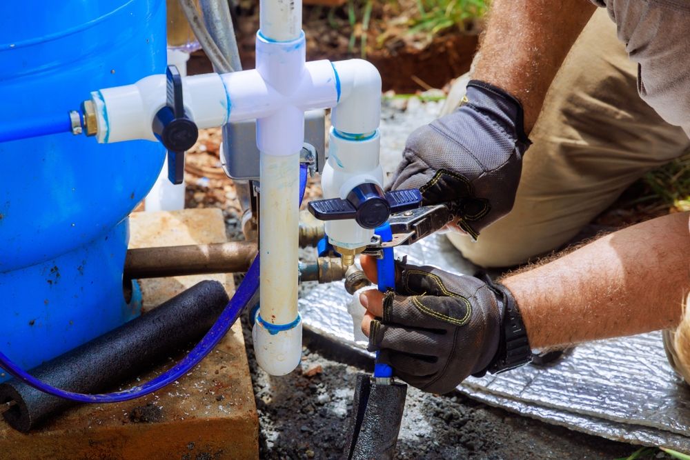 A Man is Kneeling Down Fixing a Water Pump — Clinton McArthur Plumbing in Mooloolaba, QLD