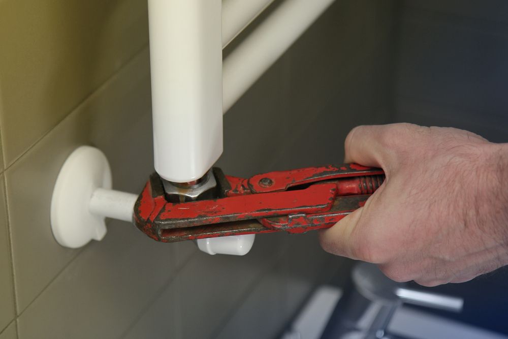 A Person is Fixing a Radiator With a Wrench — Clinton McArthur Plumbing in Buderim, QLD