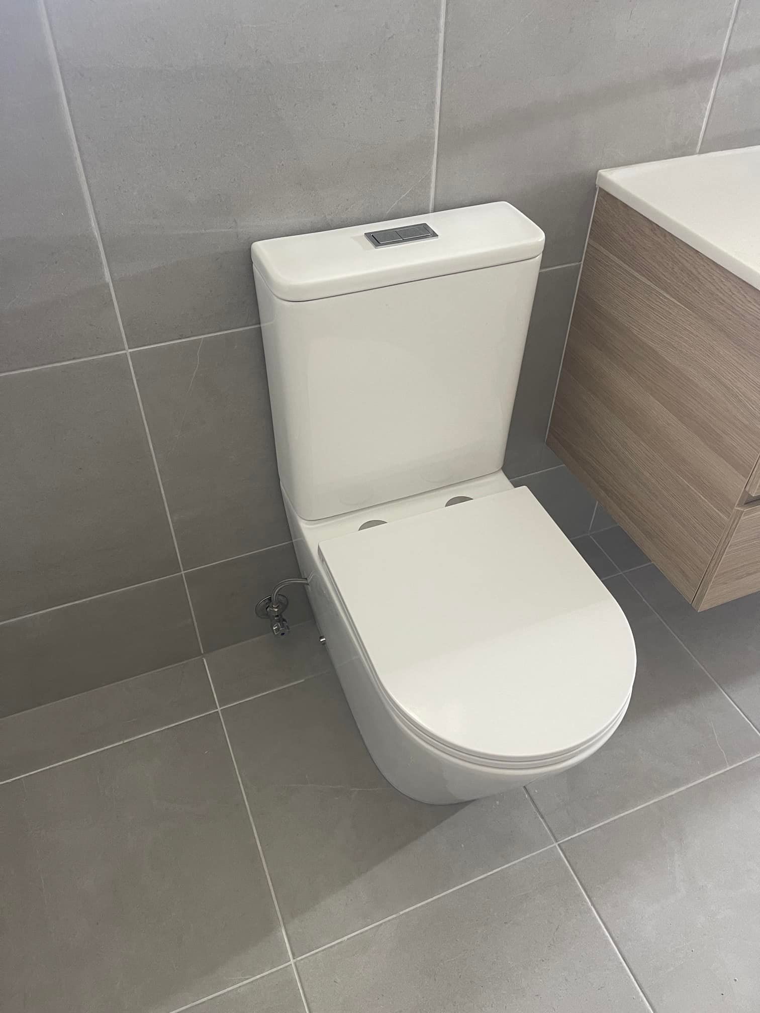 A White Toilet is Sitting in a Bathroom Next to a Sink — Clinton McArthur Plumbing in Landsborough, QLD