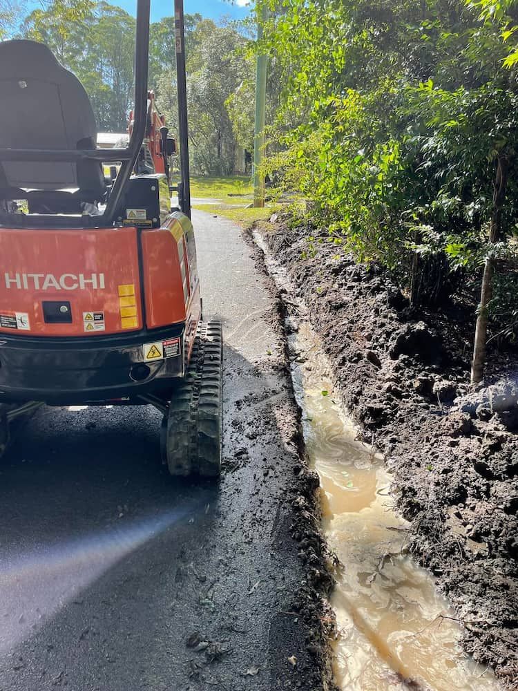 A Hitachi Excavator is Driving Down a Muddy Road — Clinton McArthur Plumbing in Landsborough, QLD