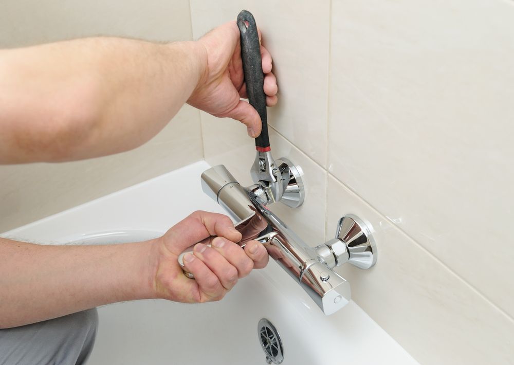 A Person is Fixing a Bathtub Faucet With a Screwdriver — Clinton McArthur Plumbing in Mooloolaba, QLD