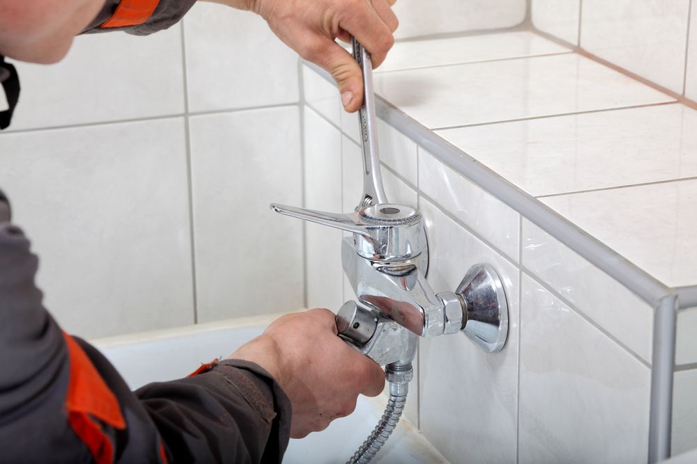 A Man is Fixing a Faucet in a Bathroom With a Wrench — Clinton McArthur Plumbing in Mooloolaba, QLD
