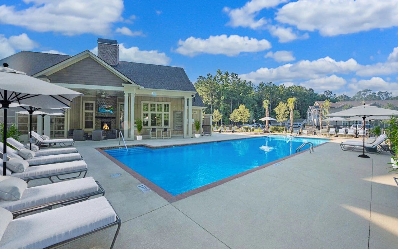 Swimming pool with lounge chairs, umbrellas, and a building under a blue sky.
