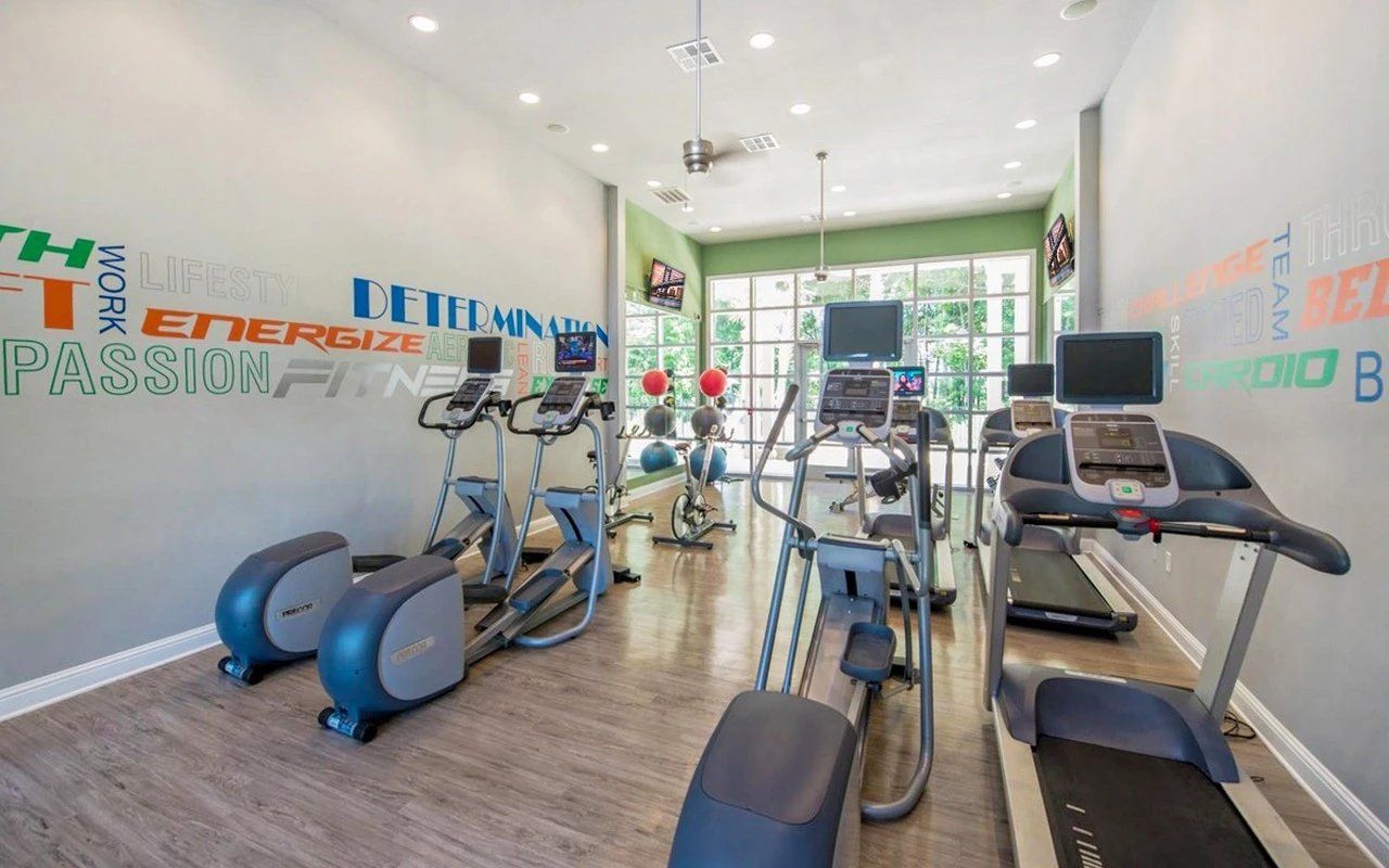 Gym with elliptical machines and treadmill; motivational words on wall; bright, open space.