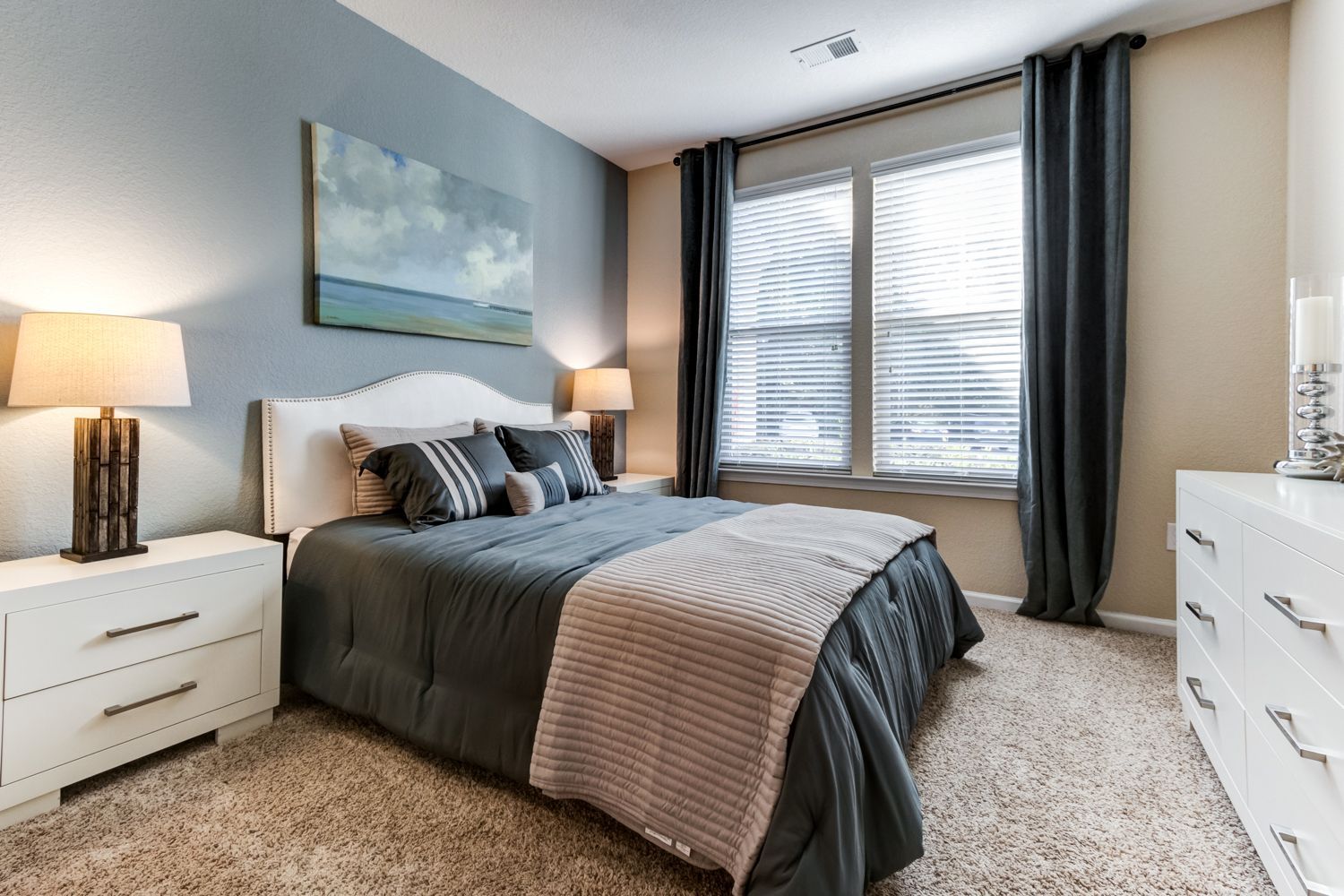 Bedroom with bed, nightstands, lamps, window, art, dresser, and carpet at The Preserve at Essex Farms, offers apartments in West Charleston, SC.