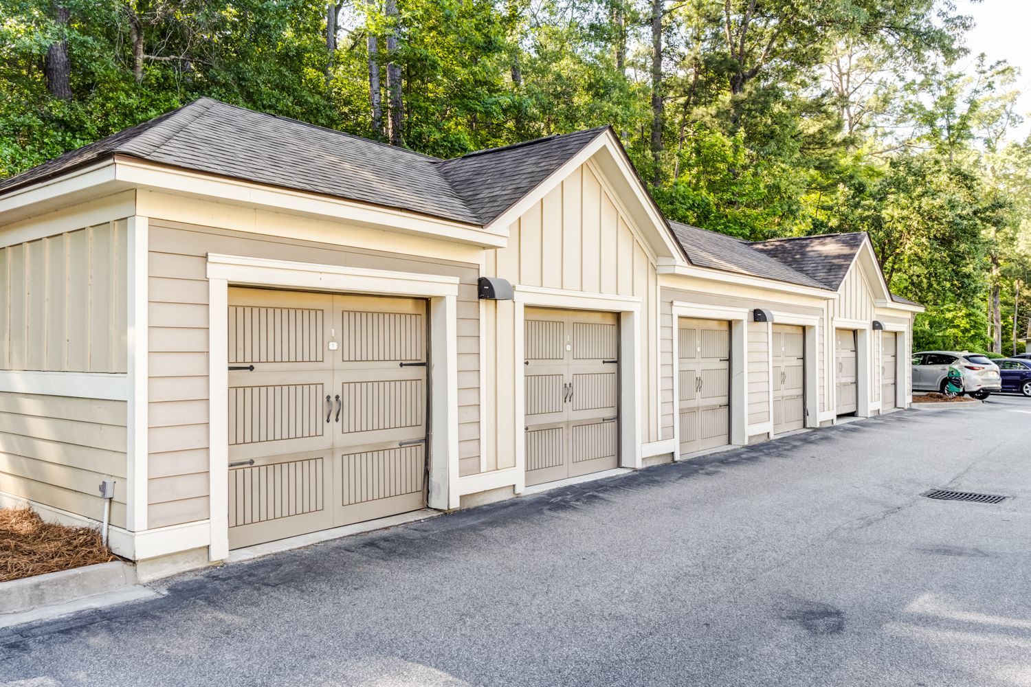 Row of beige garages with dark gray doors, asphalt driveway, trees in background at The Preserve at Essex Farms, offers apartments in Charleston, SC.