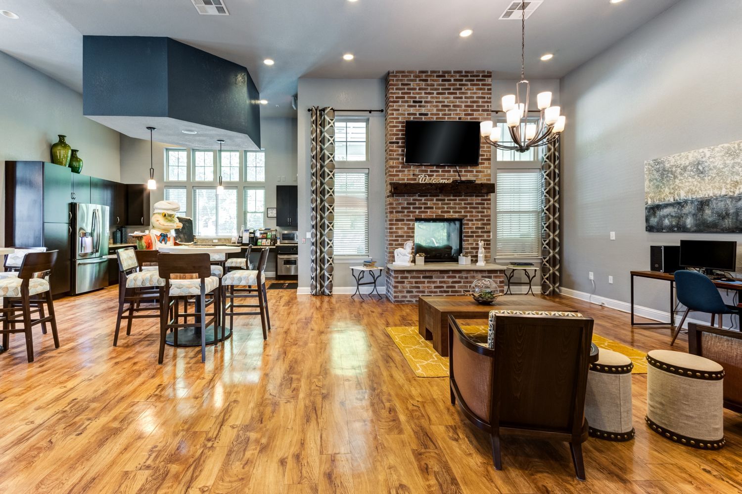 Spacious modern common room with brick fireplace, seating, kitchen, and computer desk at The Preserve at Essex Farms, offers 1, 2, and 3 bedroom apartments in Charleston, SC.