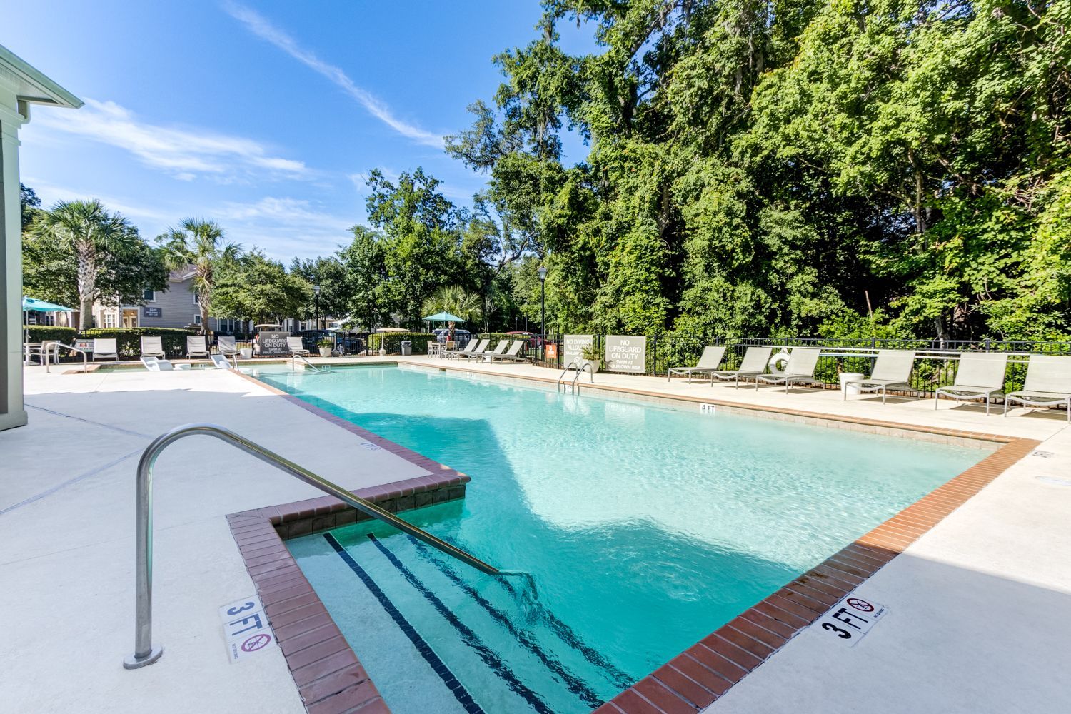 Swimming pool with blue water, surrounded by lounge chairs, next to a building and trees at The Preserve at Essex Farms, offers apartments in Charleston, SC.