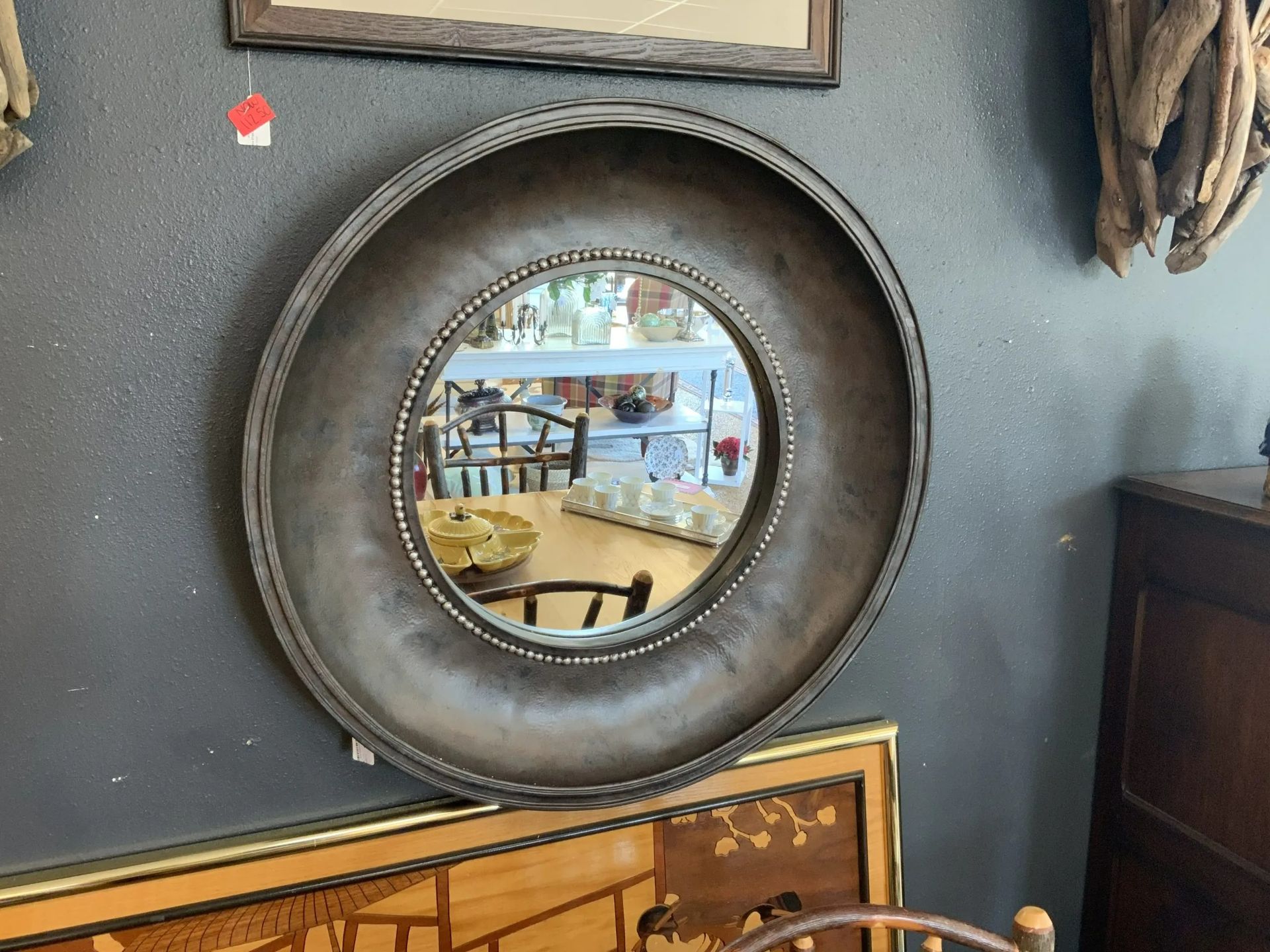 A circular wall mirror with a wide, dark, metallic frame featuring a beaded inner edge, mounted on a charcoal wall.