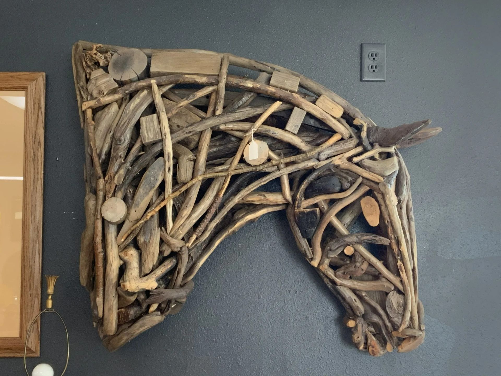 A wall-mounted sculpture of a horse head crafted from assorted driftwood and pieces of wood against a dark gray wall.