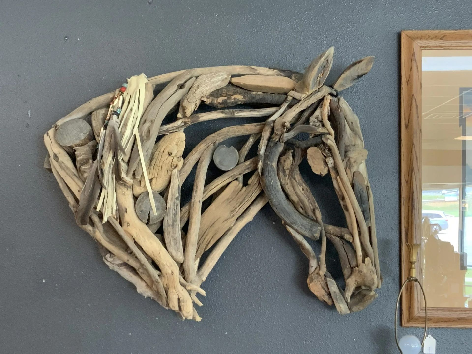 A horse head sculpture crafted from various pieces of driftwood, mounted on a dark grey wall next to a framed mirror.