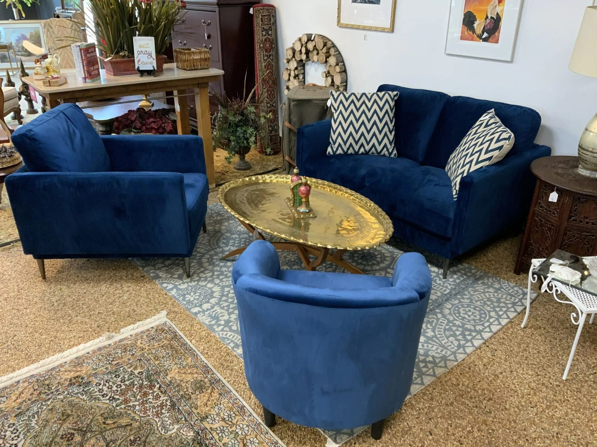 A cozy sitting area featuring two blue velvet armchairs and a matching blue loveseat with patterned pillows on a rug.