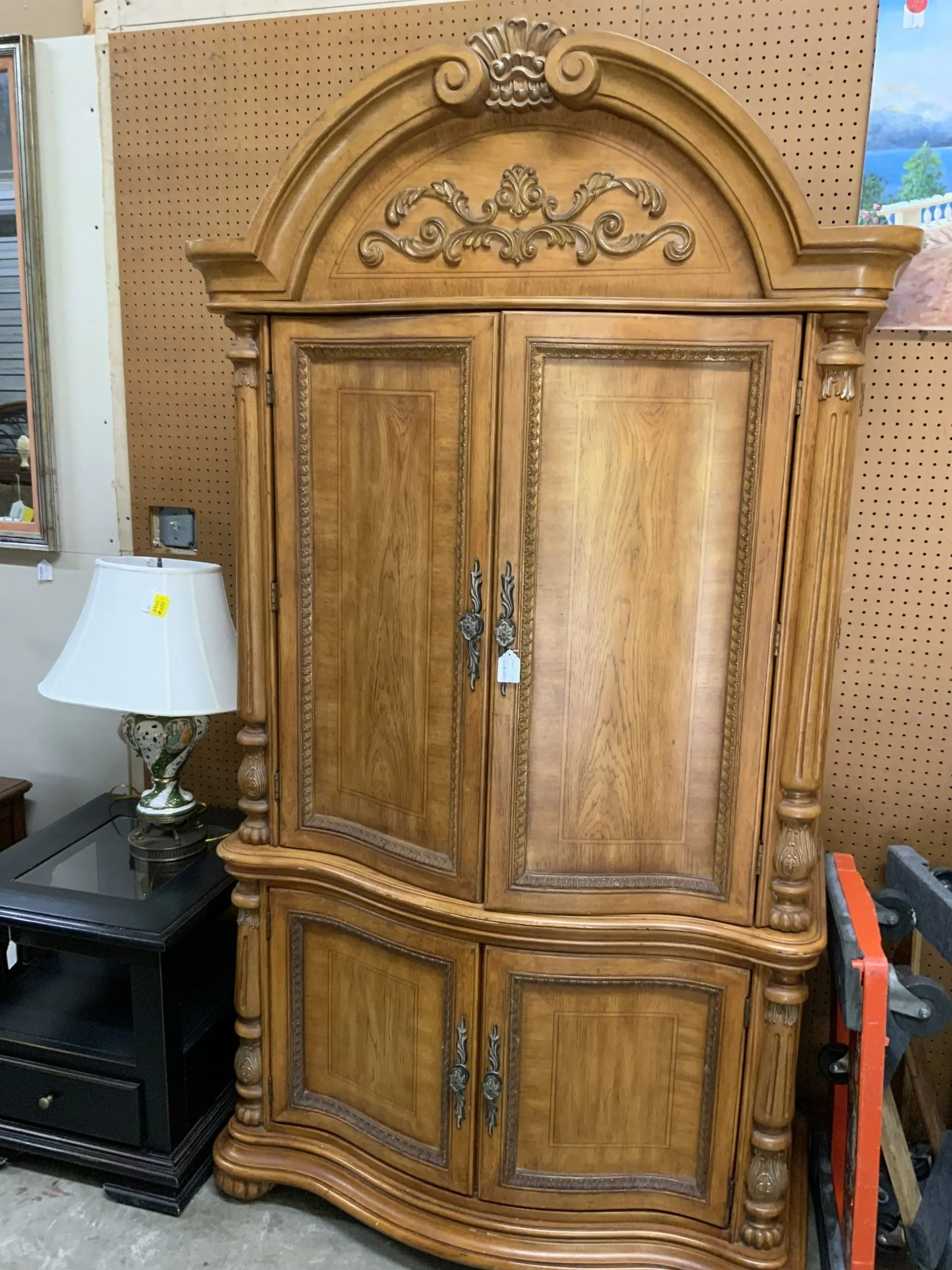 A large, arched oak armoire with decorative carvings, standing next to a small black end table and a lamp.