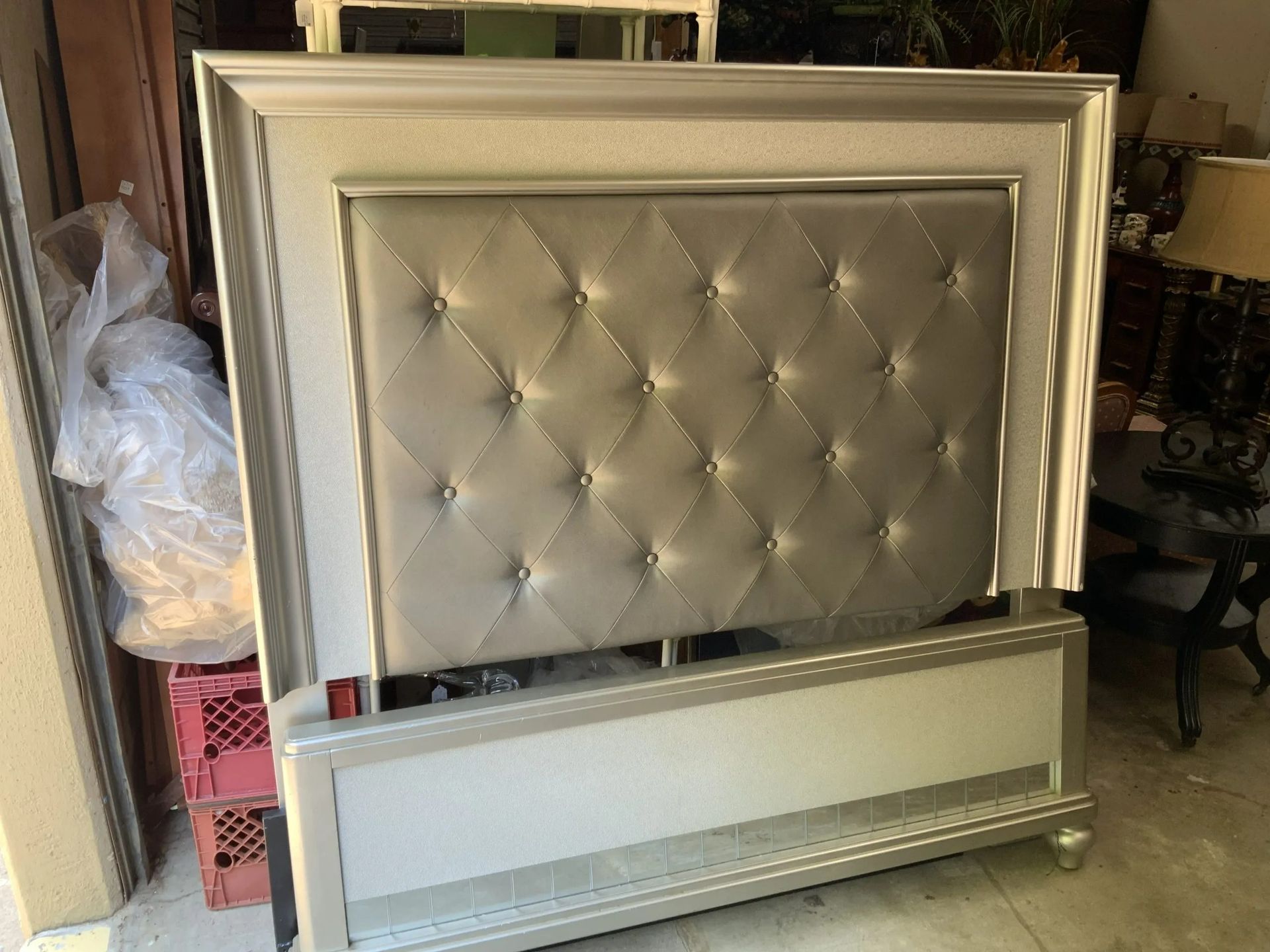 A metallic silver bed frame with a tufted, diamond-patterned upholstered headboard in a storage setting.