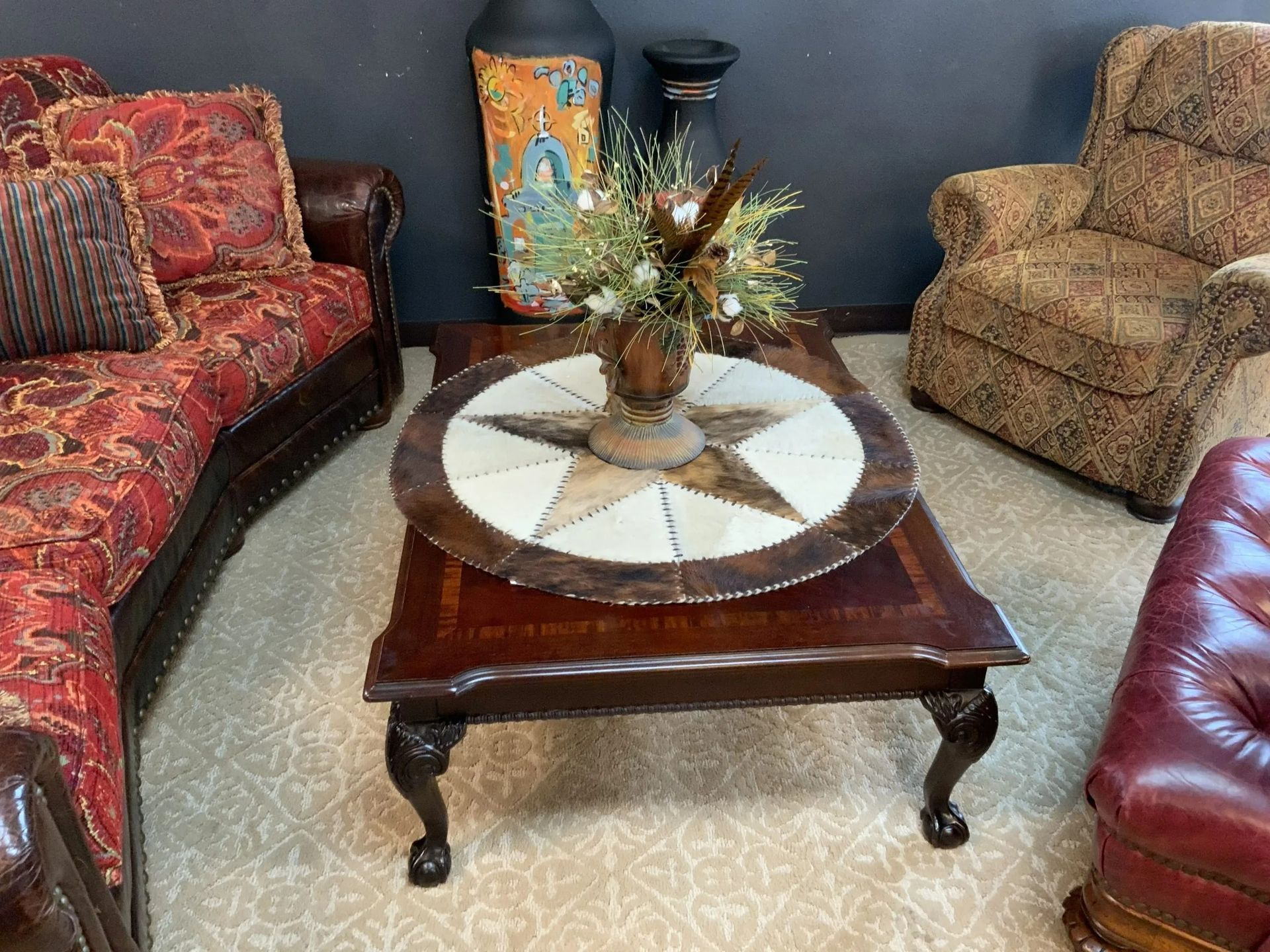 A rustic living room with a star-patterned coffee table, a red patterned sofa, a tan armchair, and a decorative vase.
