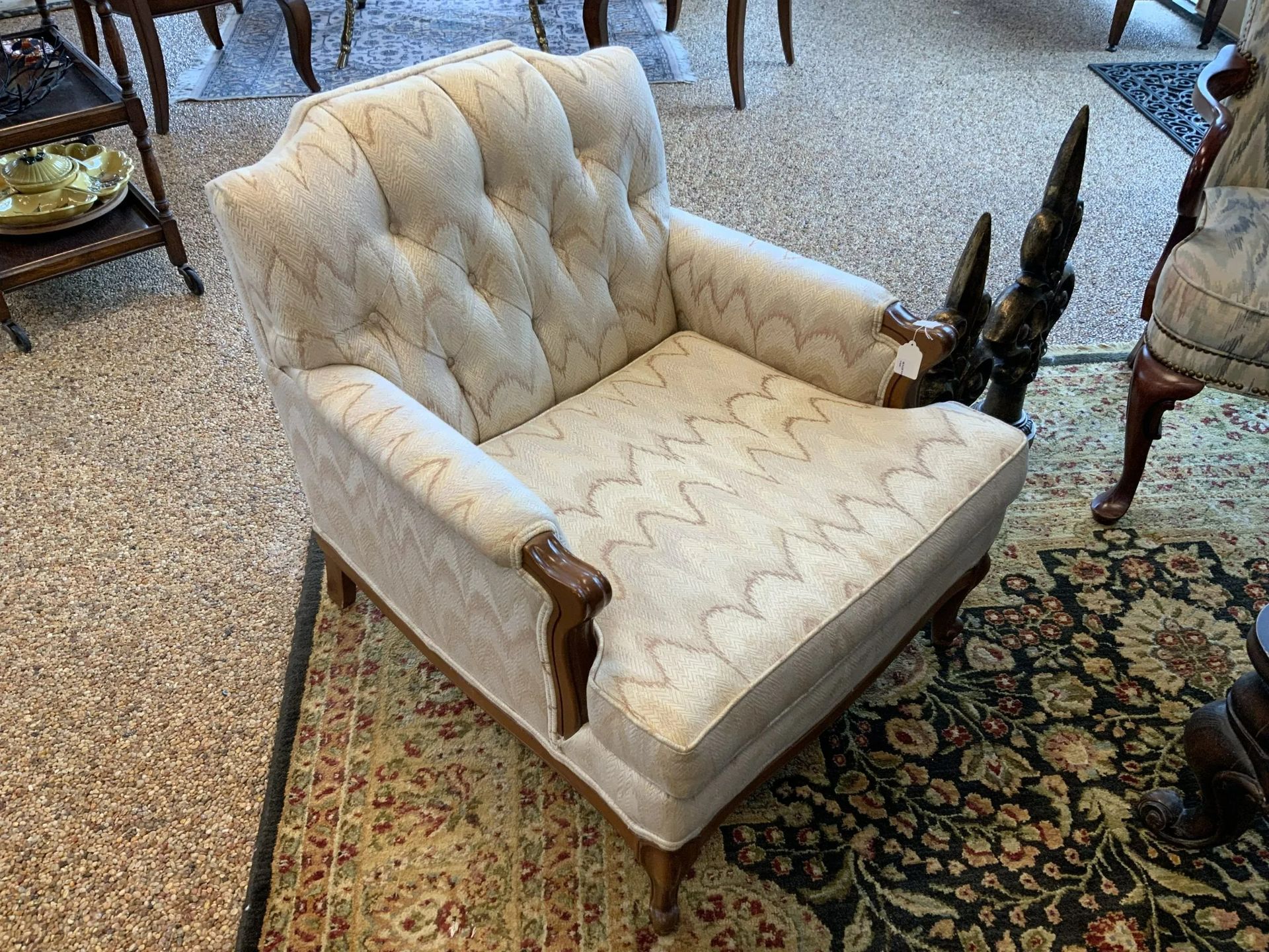 An upholstered, light-colored armchair with button tufting and decorative scalloped stitching in a furnished room.