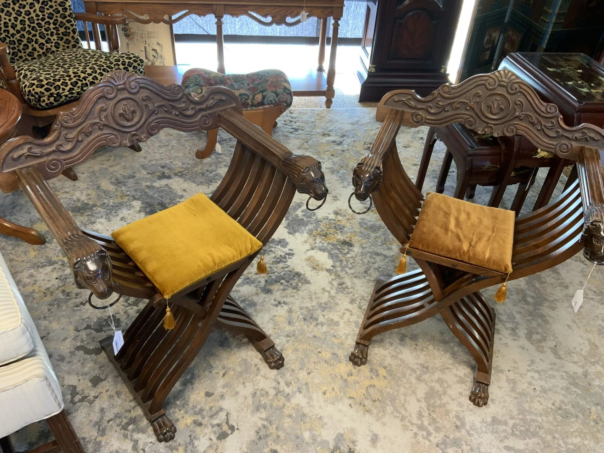 Two dark wood Savonarola-style chairs with carved lion head accents and yellow cushions, displayed in a showroom.