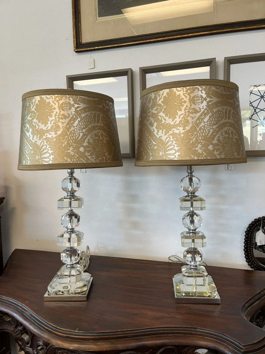 Two table lamps with stacked crystal bases and patterned gold drum shades sit on a dark wooden table.