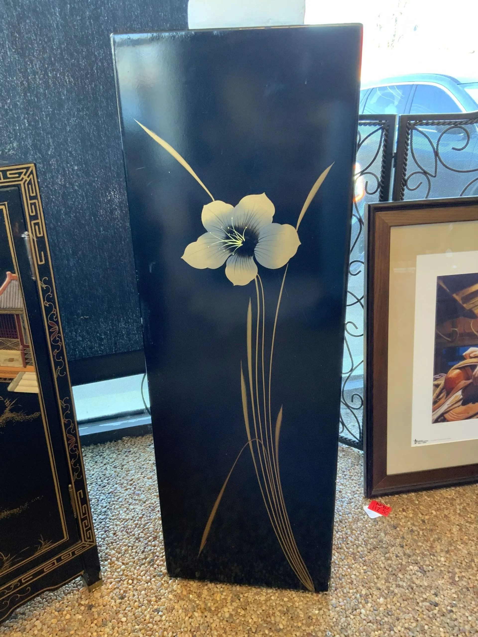 A tall, black, rectangular decorative pedestal featuring a metallic floral design on its front face.