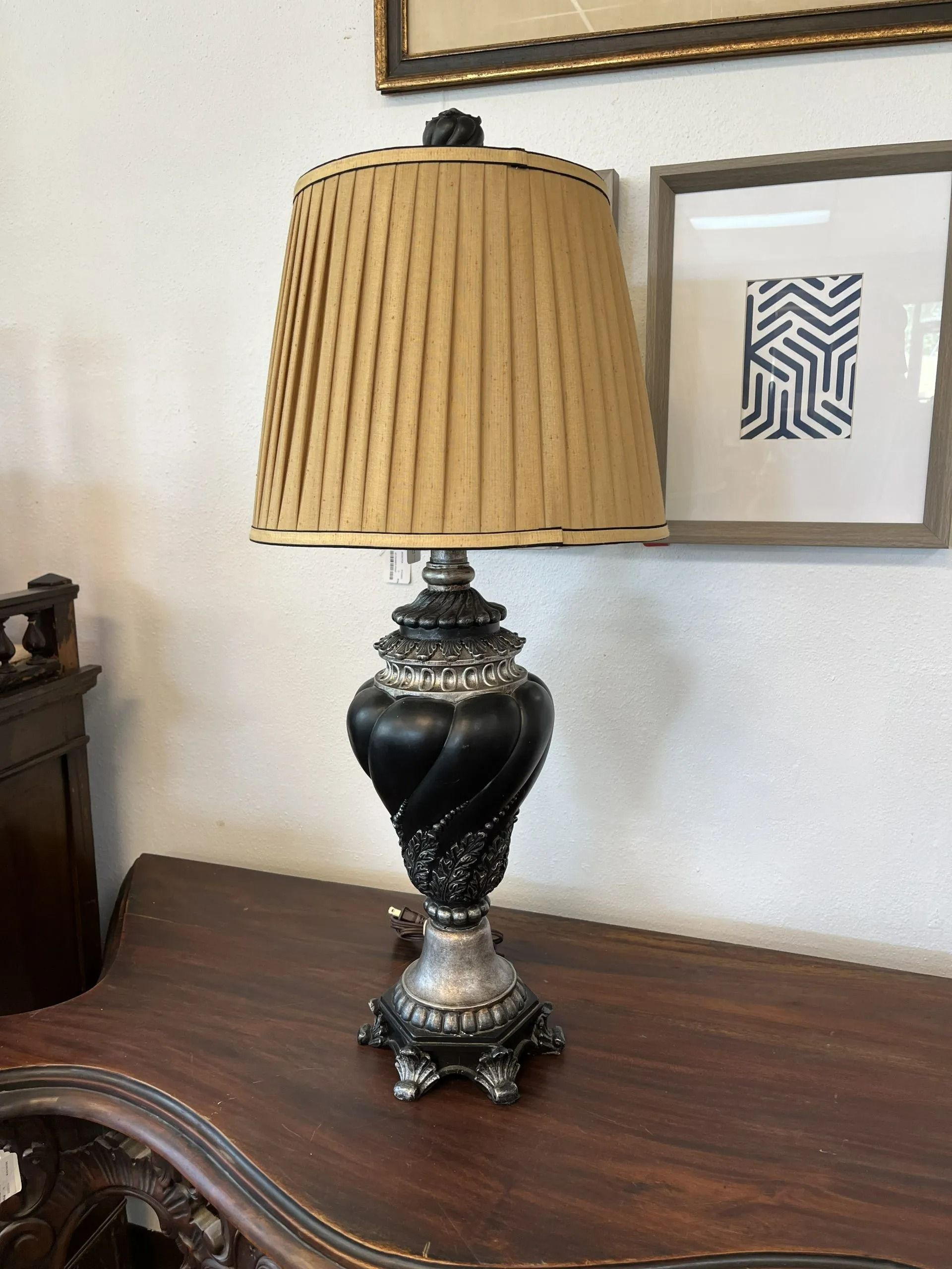 A decorative table lamp with a black, spiraled base and a pleated, tan lampshade, sitting on a dark wooden table.