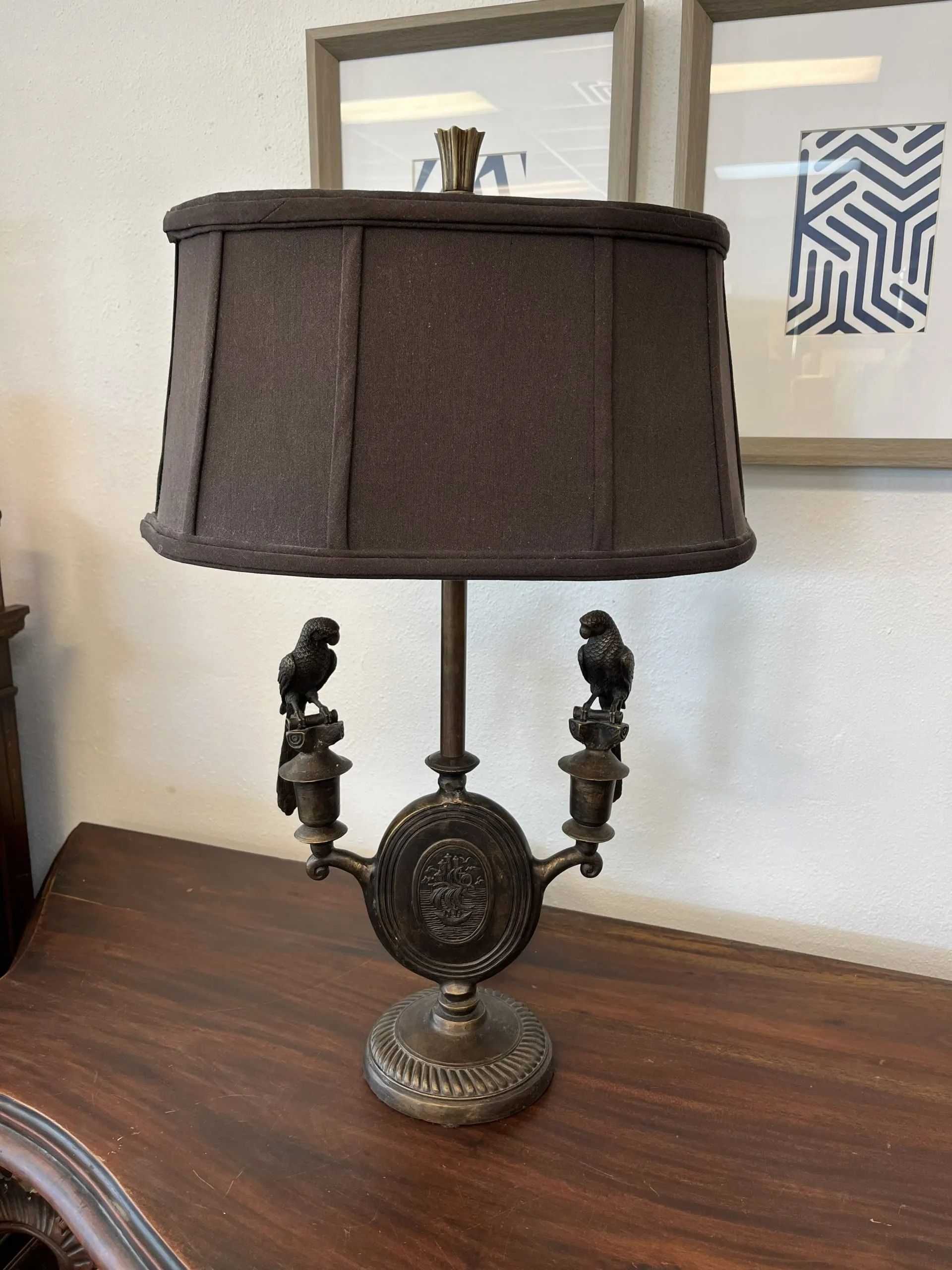 A bronze-toned table lamp with two parrot figures, an ornate central medallion base, and a dark brown pleated lampshade.