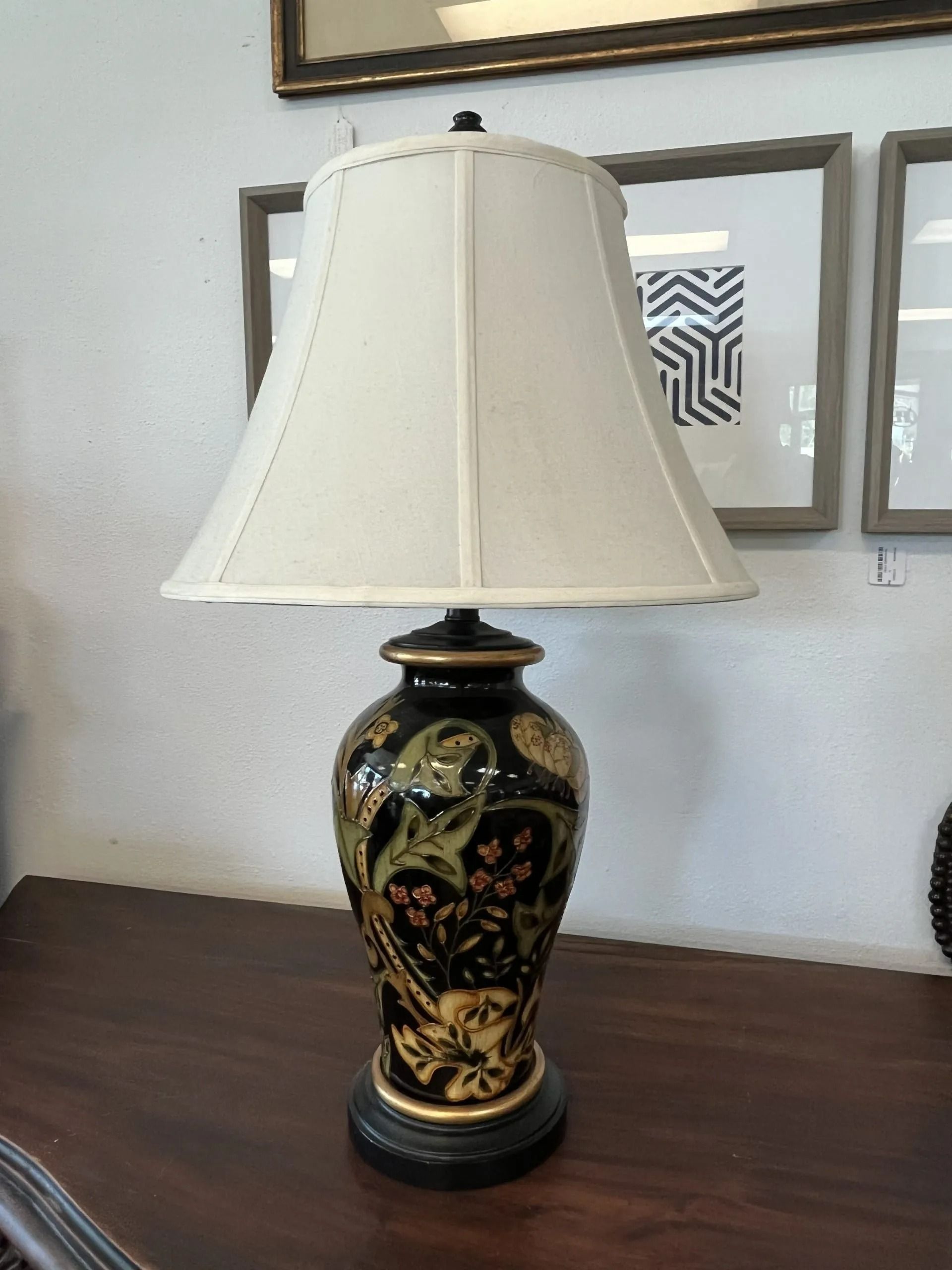 A black and gold ceramic table lamp with a cream-colored fabric shade sits on a dark wooden surface.